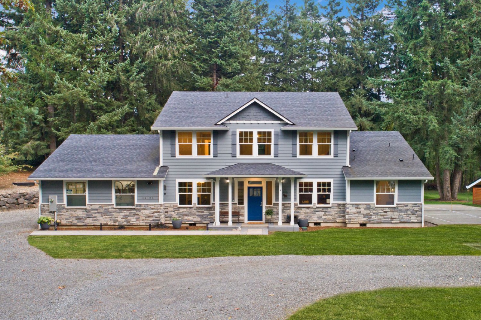Two-story blue home with a stone front and tall evergreens