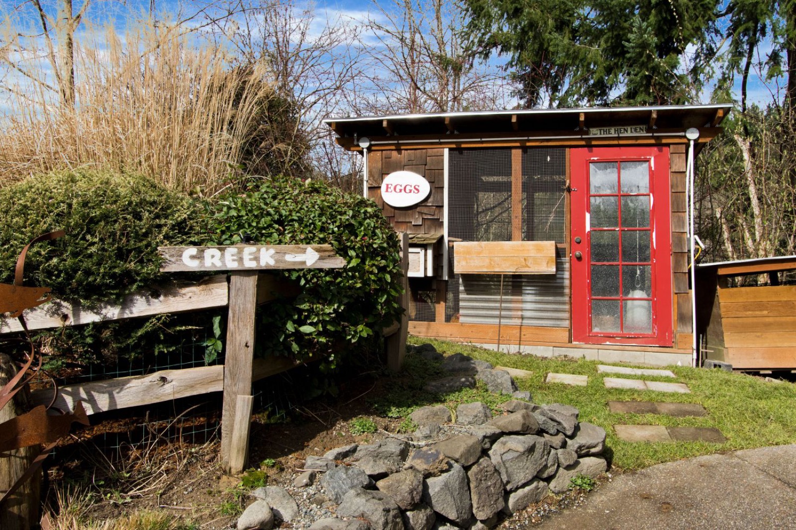 Backyard hen house with a red door beside a creek trail sign