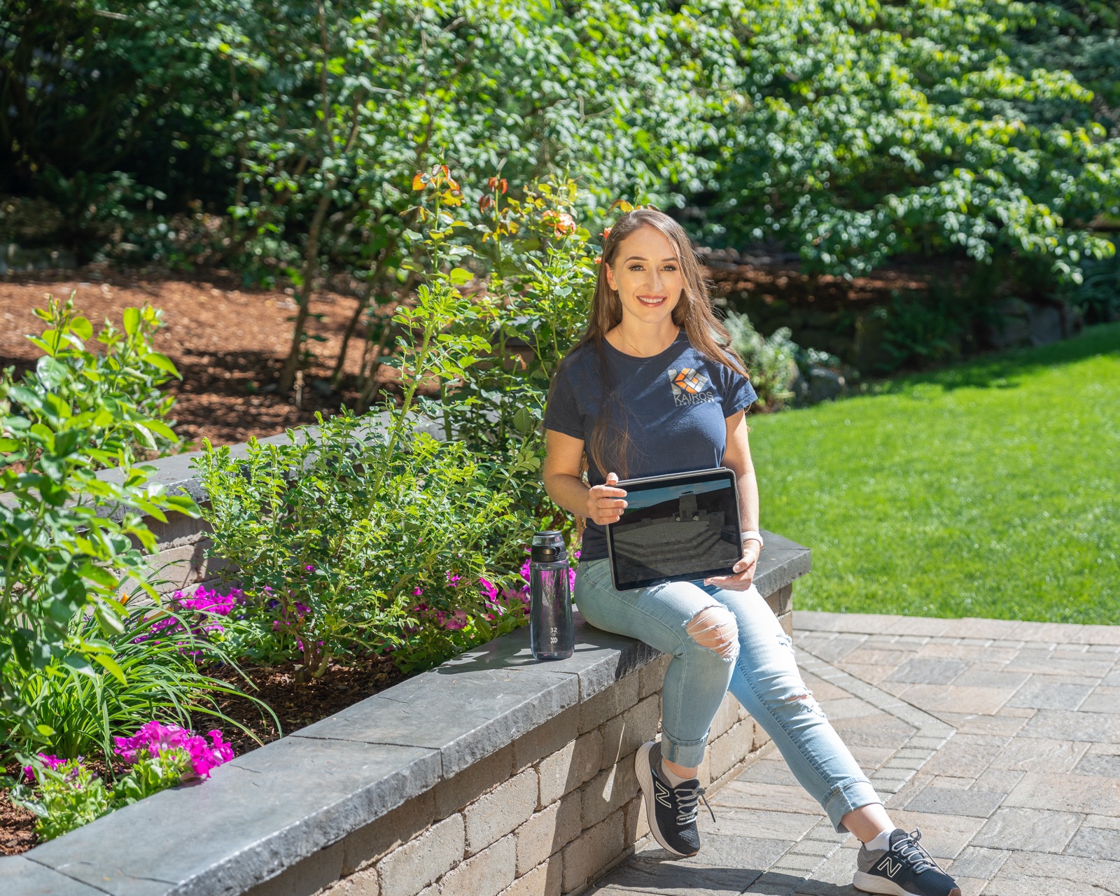 Jody sitting on a stone wall in a backyard garden
