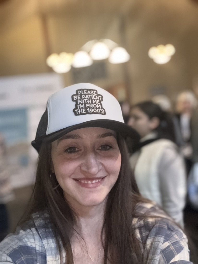 Jody smiling in a hat that reads Please be patient with me, I'm from the 1900s
