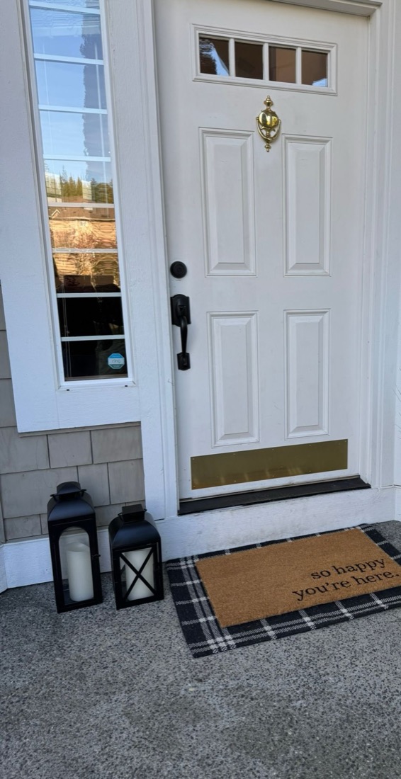 Front porch with a So happy you're here doormat and lanterns