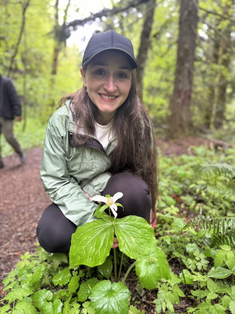 Jody kneeling beside a white trillium on the Iron Goat Trail