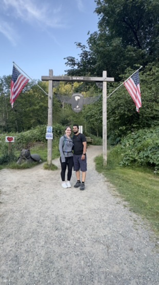 Jody at the Chirico trailhead for Poo Poo Point, under a wooden arch with American flags